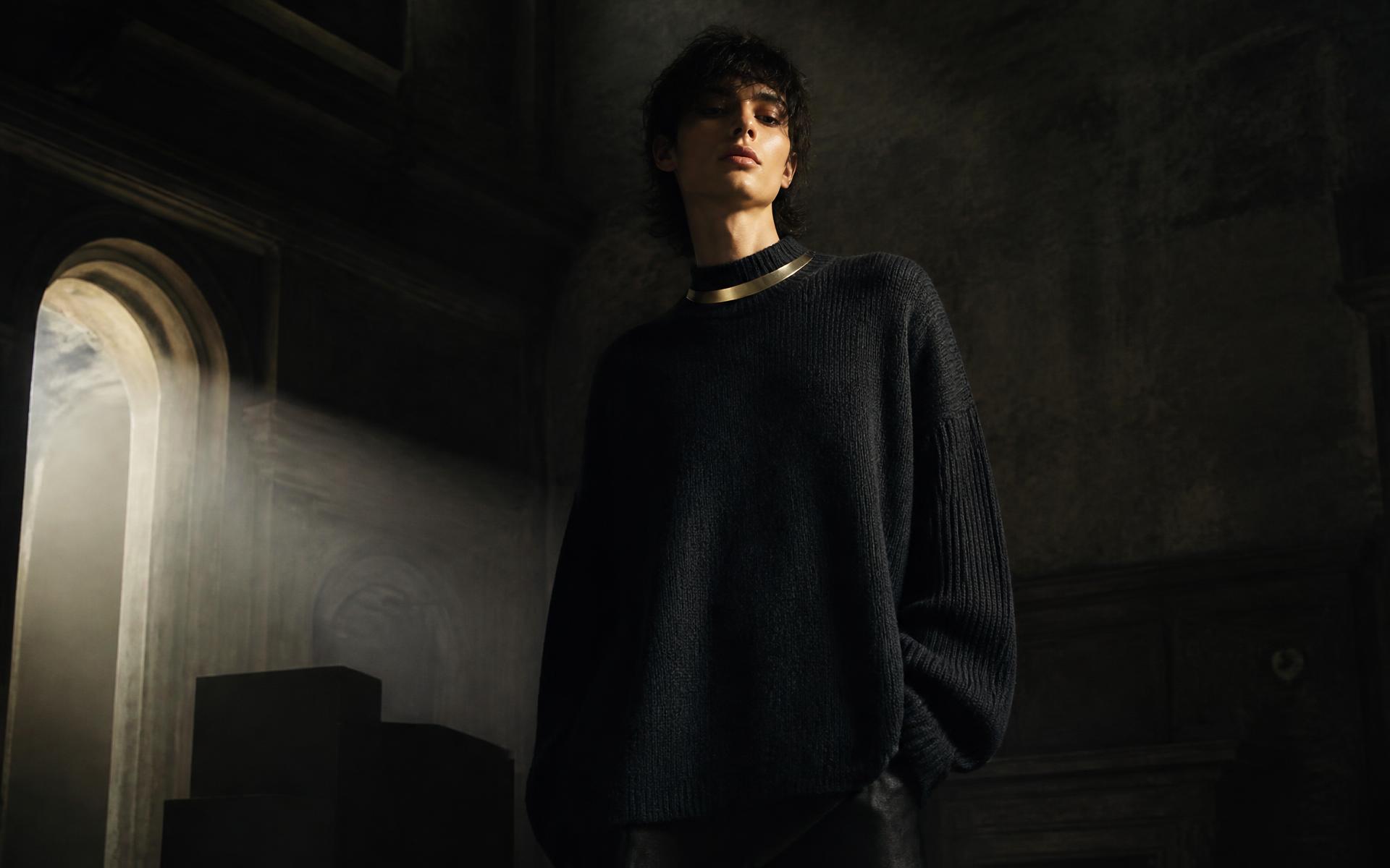 Model in a black cashmere sweater with a gold collar detail inside a dark atelier